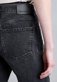 Jeans in denim neri caratterizzati da una tasca posteriore con una forma leggermente arrotondata, cuciture in contrasto e un'etichetta in pelle nera sul cinturino.