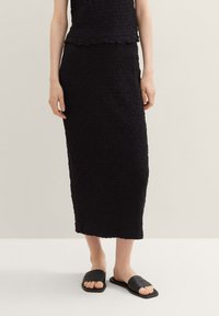 Černý texturovaný dvoudílný outfit, který se skládá z topu bez rukávů a dlouhé sukně, doplněný černými plochými sandály.