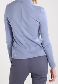 Blå figurnära långärmad topp med en mjuk textur, hög krage och strukturerade sömmar. Kombinerad med grå figurnära byxor.