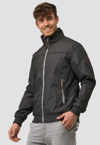 Black bomber jacket featuring a stand collar, white zipper, leather accents, plus side pockets and ribbed cuffs for comfort.