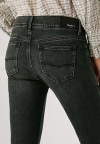 Čierne džínsy z denimového materiálu so slim fit strihom, s zadnými vreckami, kontrastným prešívaním a štítkom na páse značky. Viditeľná jemná vyblednutá textúra.