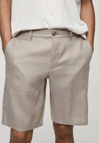 Pantalones cortos de lino beige con un ajuste relajado, que cuentan con bolsillos laterales y cierre de botón; textura suave y diseño simple y limpio.
