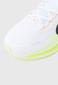 Άσπρο αθλητικό παπούτσι με επάνω μέρος από δίχτυ, πορτοκαλί και πράσινες λεπτομέρειες, μαύρο λογότυπο και ανάγλυφη σόλα για πρόσφυση. Ορατό λογότυπο στο πλάι.