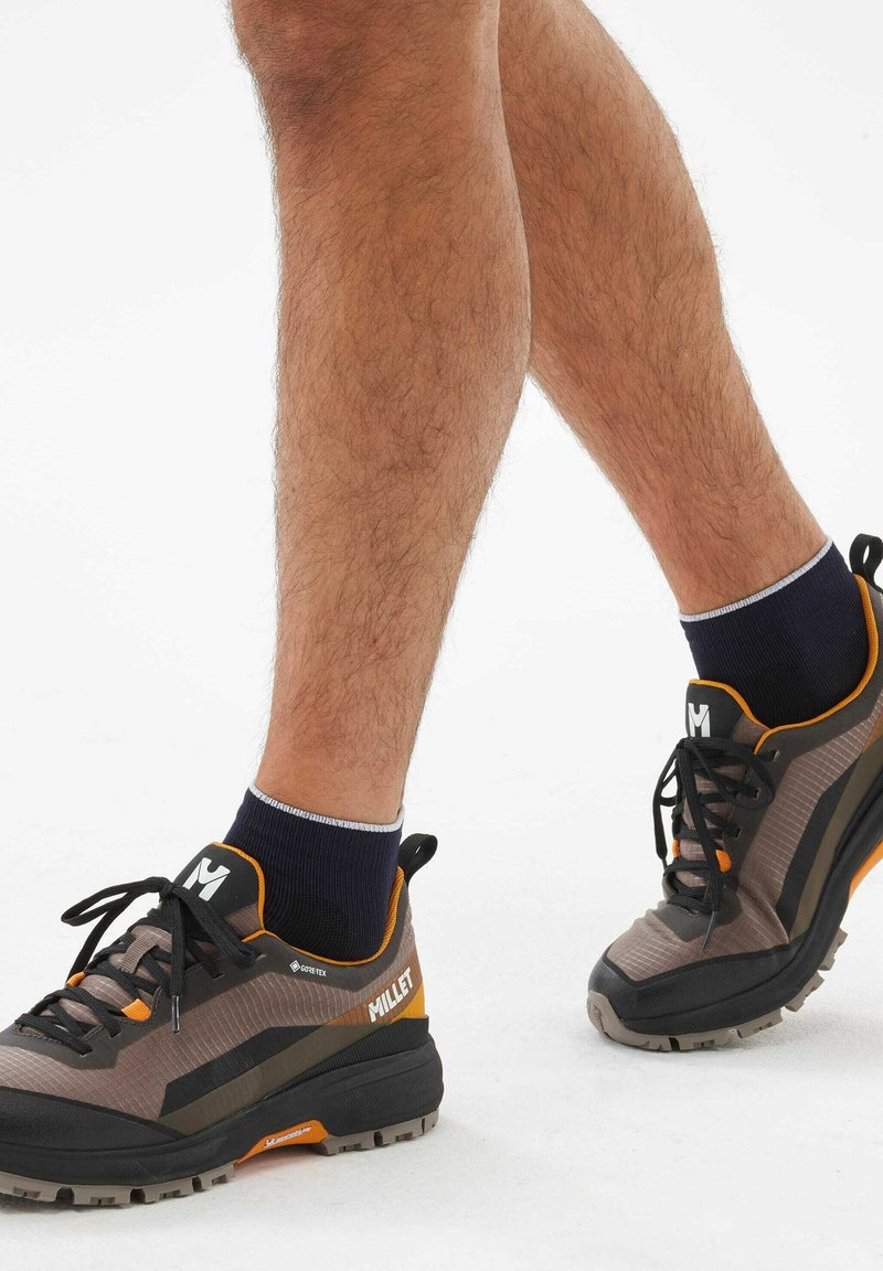 Chaussures de randonnée GORE-TEX en gris et noir avec des accents orange. Elles présentent un dessus texturé, une semelle rembourrée et des lacets noirs.
