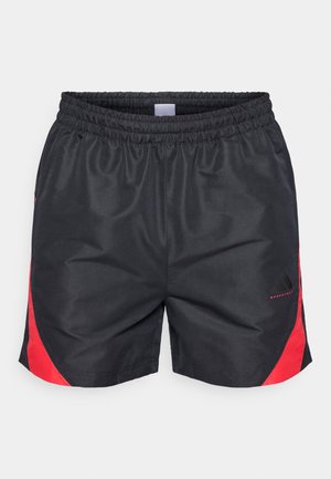 Shorts de sport noirs avec accents rouges sur les côtés, taille élastique, tissu synthétique lisse, et un logo imprimé sur le bas à l'avant.