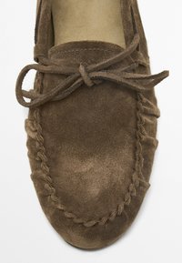 Braune Wildleder-Mokassins mit runder Zehenpartie, abgerundeten Kanten, Schnürdetail und dekorativen Nähten an den Seiten. Weicher Stoff und minimalistisches Design.