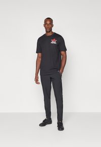Svart bomullströja med röd "ADIDAS FOOTBALL" grafik på bröstet, ihopparad med eleganta svarta träningbyxor och sportiga svarta skor.