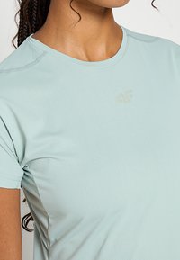 Jasnoniebieska sportowa koszulka z krótkim rękawem, wykonana z oddychającego materiału. Posiada delikatny, teksturowany wzór oraz małe, wytłoczone logo na klatce piersiowej.