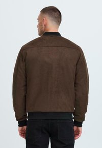 Braune Wildleder-Bomberjacke mit ribbeligem schwarzem Kragen und Bündchen, ausgestattet mit einer glatten Textur und geradem Schnitt.