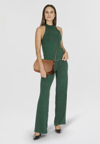 Grünes ärmelloses Oberteil und passende ausgestellte Hose aus Strickstoff. Braune Umhängetasche mit strukturiertem Finish und abnehmbarem Riemen.