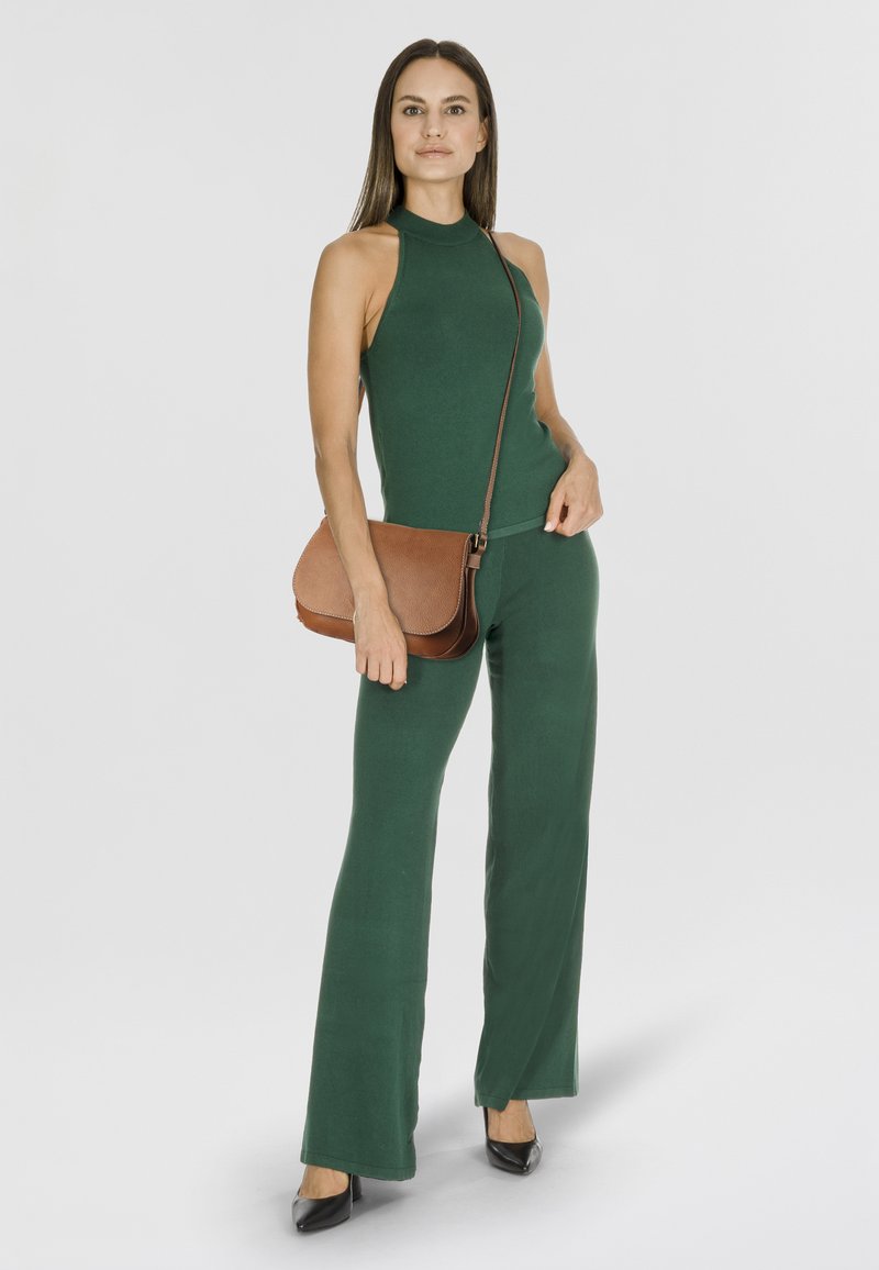 Grünes ärmelloses Oberteil und passende ausgestellte Hose aus Strickstoff. Braune Umhängetasche mit strukturiertem Finish und abnehmbarem Riemen.