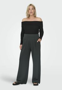 Schwarzes, schulterfreies Ripp-Top kombiniert mit hoch taillierten, dunkelgrünen, weit geschnittenen Hosen mit Seitentaschen und einer glatten Textur.