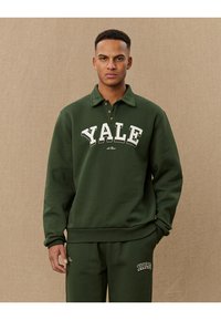 Dark green sweatshirt with a collared neckline, featuring "YALE" in white lettering across the chest and ribbed cuffs and hem.