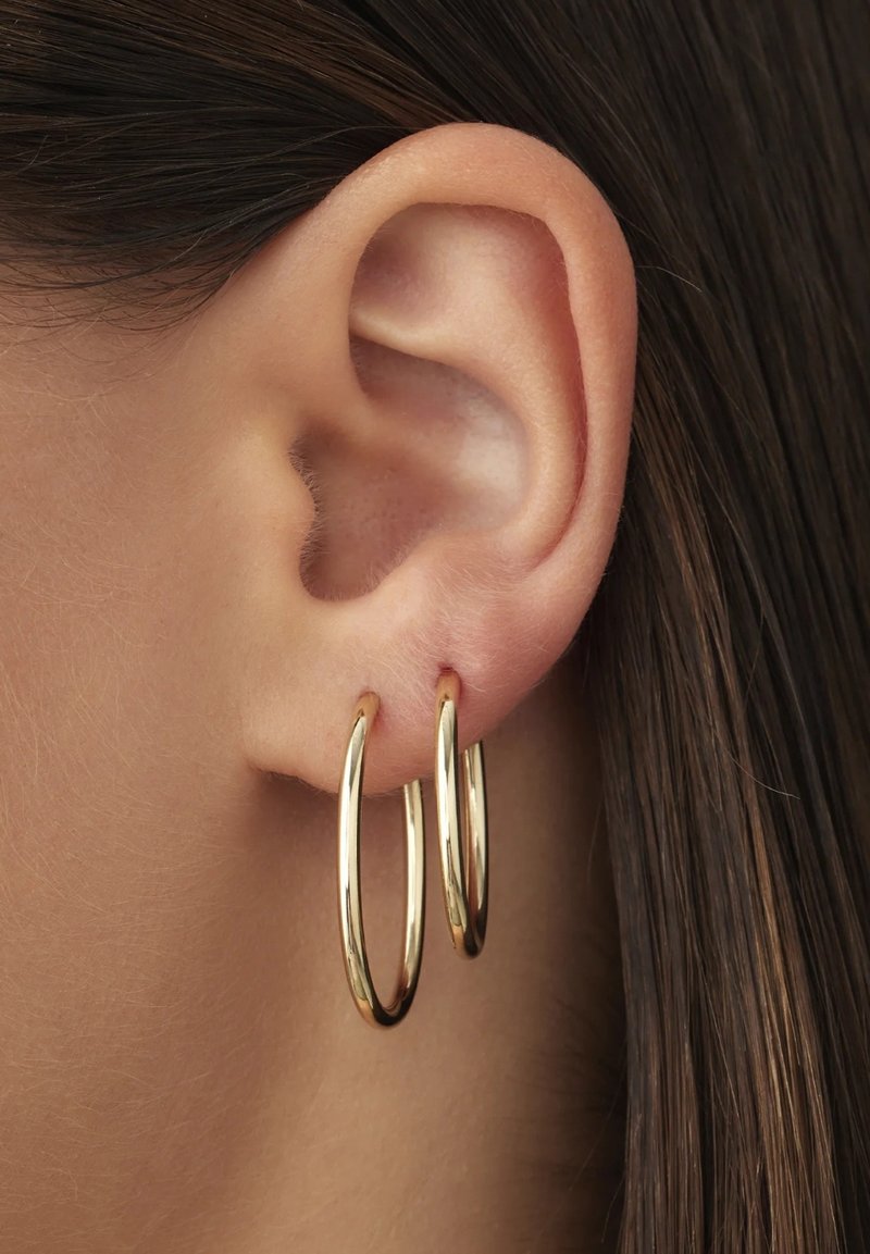Des boucles d'oreilles en or en forme de créoles, présentées sur le lobe d'une oreille, avec une surface lisse et brillante et une forme circulaire classique.