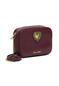 Borsa a tracolla in pelle bordeaux con un'ornamento a forma di cuore dorato, zip superiore e tracolla a catena. Presenta un logo impresso sul davanti.