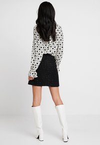 Svart-och-vit skjorta med stjärnmönster, svart strukturerad kjol och vita knähöga stövlar. Bakifrån med långt vågigt hår synligt.