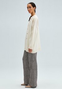 Cream oversized cardigan with button closure and ribbed hem, paired with wide-leg plaid pants in black, white, and hints of red.