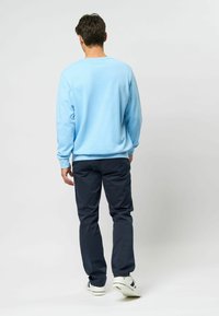 Vaaleansininen collegepaita, pyöreä pääntie, teksturoitu kangas. Yhdistetty tummansinisiin housuihin, jotka ovat vyötäröltä istuvat ja lahkeista kapenevat. Valkoiset tennarit, joissa on korostuksia.