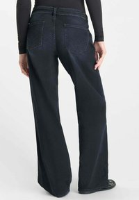 Jeans en denim foncé à jambes larges avec une taille haute, dotés de deux poches arrière avec un détail de couture unique. Texture lisse et coupe décontractée.