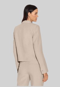 Beige op maat gemaakte blazer met een cropped ontwerp, lange mouwen en knoopaccenten op de manchetten. Gemaakt van gestructureerde stof met een gladde afwerking.