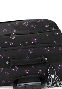 Valigia nera con un motivo floreale in viola e rosa. Presenta un manico retrattile e un portachiavi a forma di scimmia nera.