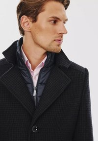 Czarny checkered płaszcz z klapami, noszony na niebieskiej pikowanej kamizelce i jasnoróżowej koszuli. Posiada zapięcie na guziki i zamek.