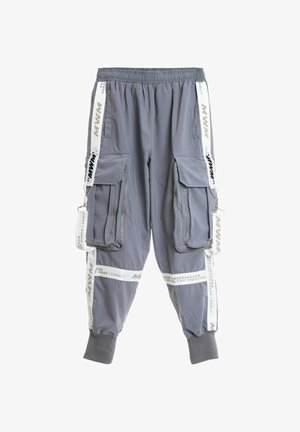 Pantalones cargo grises con puños elásticos, múltiples bolsillos con cremallera y solapa, y tiras decorativas blancas con texto a lo largo de los laterales y las piernas.
