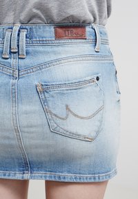 Ljusblå denim mini kjol med bakfickor och brun LTB-märkesetikett, bärs med en grå topp instoppad.