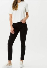 Camiseta blanca de algodón combinada con jeans negros ajustados. Lleva puestas unas zapatillas blancas con detalles en beige claro. Un atuendo simple y casual.