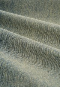 Tela de mezclilla azul claro con una textura suave, que muestra un sutil patrón de tejido y ligeras variaciones en el tono a lo largo de la superficie.