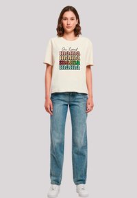 Cream short-sleeve t-shirt featuring colorful "mama" text in various fonts. Paired with light blue straight-leg jeans and white sneakers.