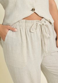 Byxor i linblandning i ljus beige med elastisk midja, dragsko och sidofickor; texturen verkar mjuk och något skrynklig.