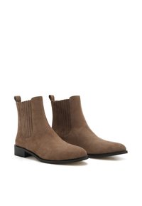 Bottines en suède marron avec des panneaux latéraux élastiques, une texture lisse, un bout pointu et un petit talon carré. Présente des coutures verticales subtiles.