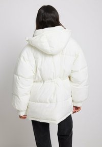 Chaqueta acolchada blanca con capucha, presenta una cintura ajustada y un diseño acolchado. Material suave y liso; mangas largas y oversized; ajuste casual.