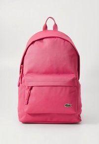 Ružový batoh vyrobený z odolnej tkaniny, s predným vreckom na zips, nastaviteľnými popruhmi a malým logom. Hladká textúra a zaoblený tvar.