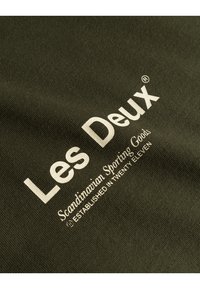 Olive green fabric with a smooth texture featuring white printed text: "Les Deux," "Scandinavian Sporting Goods," and "Established in Twenty Eleven."