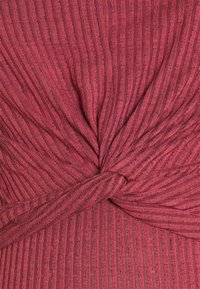 Tessuto a costine di un rosso profondo, con un dettaglio a nodo attorcigliato al centro per una maggiore texture e dimensione. Materiale morbido e elasticizzato.