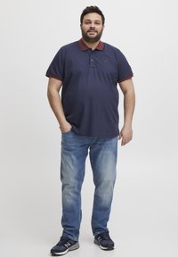 Marineblå polo skjorte med maroon krageaksenter, kombinert med lyseblå jeans. Antrekket er fullført med marineblå joggesko.