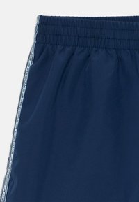 Calções atléticos azul marinho com cintura elástica e faixa lateral com texto "SWOOSH" repetido e logotipo da Nike.