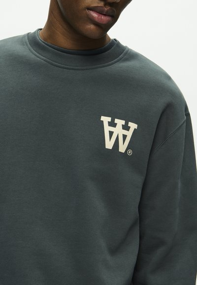 Sweatshirt vert foncé avec col côtelé, présentant un grand logo blanc sur la poitrine. Fabriqué dans un tissu doux et texturé.