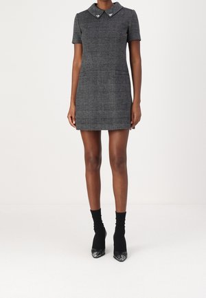 Gråternet kort kjole med krave og lommer, struktureret design, parret med sorte ankelstrømper og hæl-sko.