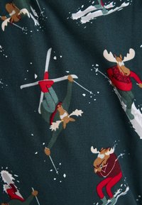 Groene stof met elanden die skiën in rode en witte outfits, met sneeuwaccenten. Het ontwerp bevat speelse houdingen en fantasierijke details.