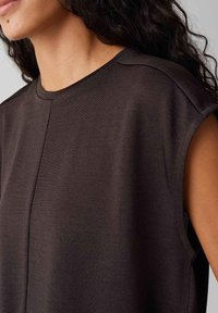 Korte bruine top met korte mouwen van ribstof. Heeft een ronde hals en een ingetogen ontwerp met subtiele naden op de schouders.