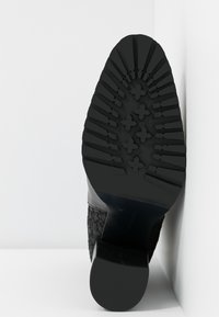 Semelle de botte noire à talon avec des rainures profondes et un motif croisé. Fabriquée en caoutchouc, avec un côté texturé et une base de talon lisse.