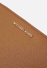 Clutch in pelle marrone con texture, logo dorato 'MICHAEL KORS' e chiusura con zip, caratterizzato da una finitura a pelle di pesca e un design elegante.