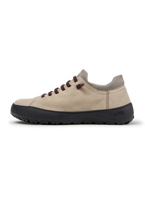 Beżowy niski sneaker z dzianym kołnierzem wokół kostki, ciemnobrązowymi sznurowadłami, czarną grubą gumową podeszwą i boczną pętelką do ściągania.