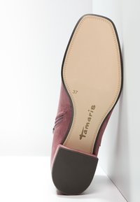 Scarpa in camoscio rosa con punta arrotondata e dettaglio con cerniera. La suola è piatta, con una leggera texture in gomma, e il nome del marchio "Tamaris" è visibile.