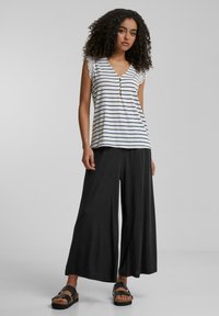 Top sans manches rayé en blanc et marine, avec un col en V et des accents en dentelle. Associé à un pantalon large noir et des sandales plates.