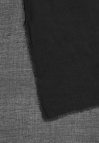 Tissu en lin noir drapé sur un fond gris texturé, montrant un bord à frange pour un détail supplémentaire.