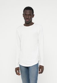 Witte lange mouwen t-shirt met een ronde hals, met een gladde textuur en een ontspannen pasvorm, gecombineerd met blauwe jeans.